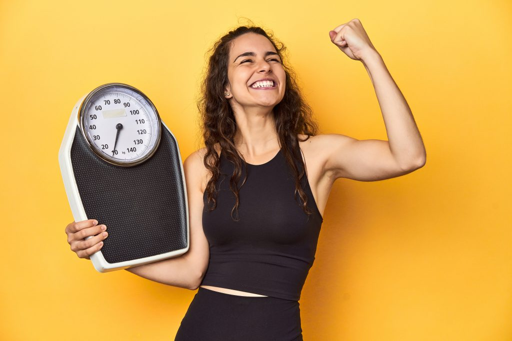 Woman celebrating healthy weight loss with a scale — GLP-1 medication program in Napa